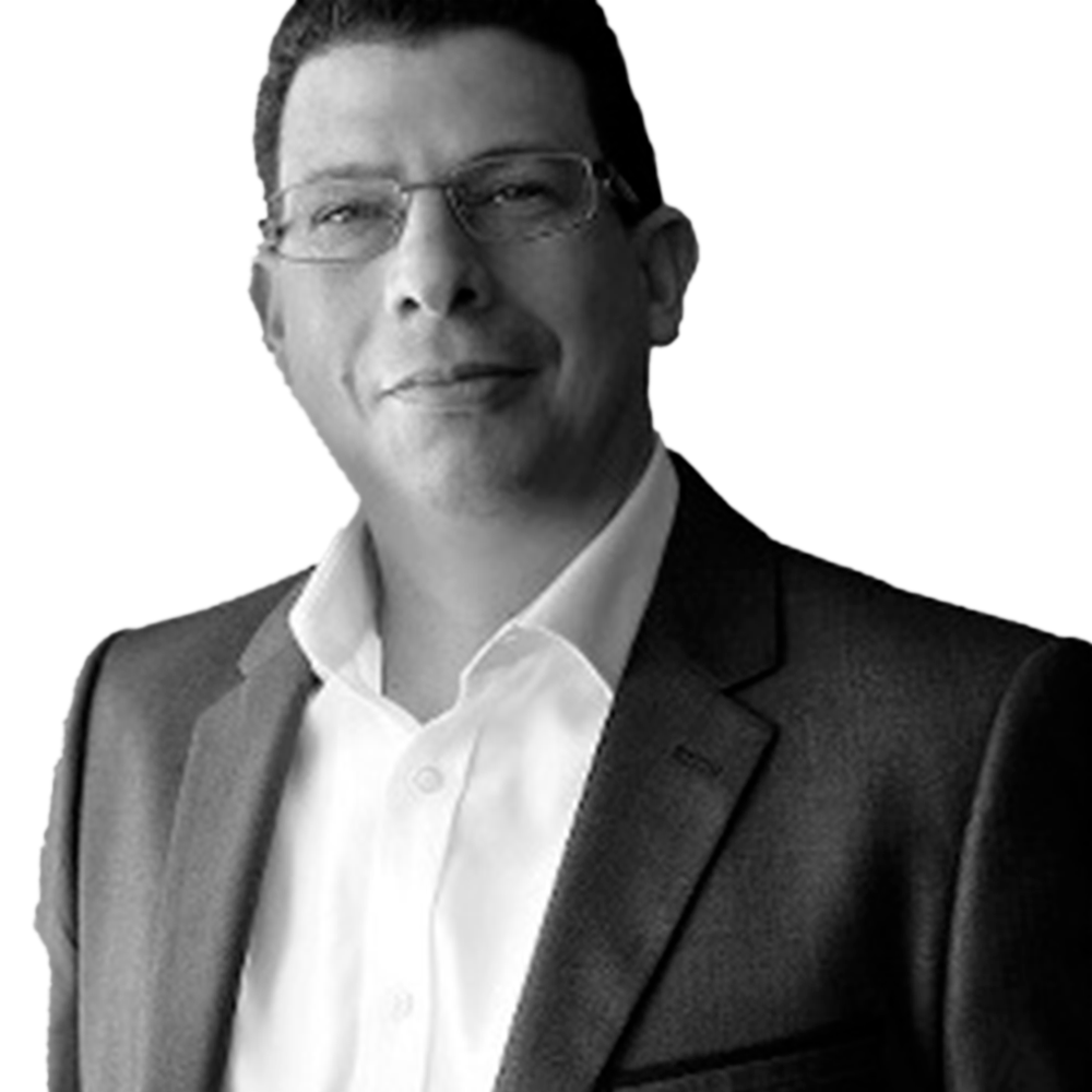 Profile picture of a person with short hair and a beard, wearing a black vest and white shirt, with a blurred outdoor background